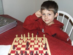 Noah at eight years old, seated at a table with a chessboard.