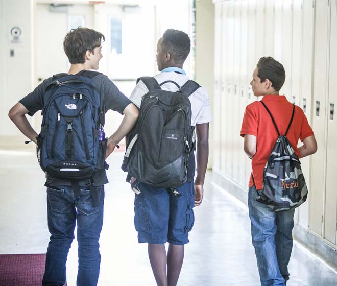 3 Middle School boys walking in a school hallway with backpacks