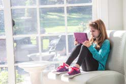 Young girl sitting alone at home on a sofa with tablet, reading