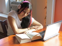 Photo of high-school student with laptop, headset and a book sitting at the table, studying