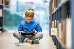 Student Reading Audiobooks in Library