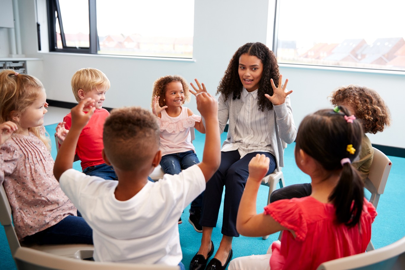 Teacher with kids sitting on chairs in circle and holding hands up